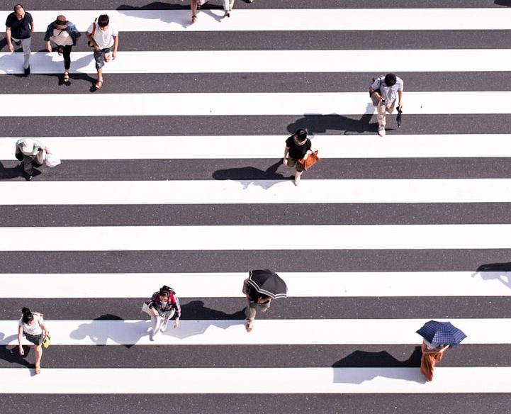 Zebrasteifen mit Menschen; Foto: Ryoji Iwata von Unsplash Weiß-grauer Zebrastreifen mit Menschen, von oben fotografiert